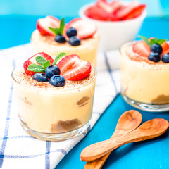 homemade, exquisite dessert tiramisu in glasses decorated with strawberry, blueberry, mint on blue wooden table