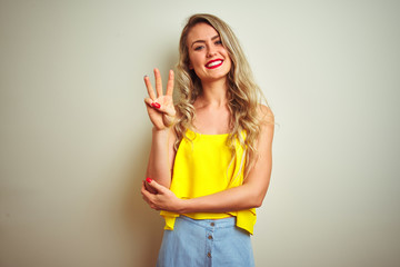 Young beautiful woman wearing yellow t-shirt standing over white isolated background showing and pointing up with fingers number three while smiling confident and happy.