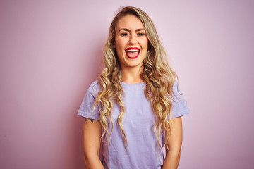 Young beautiful woman wearing purple t-shirt standing over pink isolated background sticking tongue out happy with funny expression. Emotion concept.
