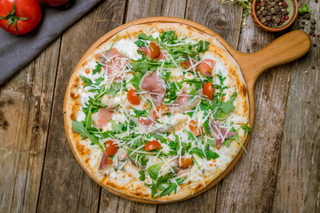 Pizza with Parma ham and arugula on wooden table