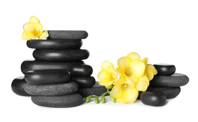 Stack of black spa stones and fresh flowers isolated on white