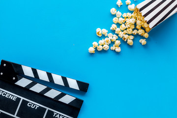 Watch film in cinema with popcorn and clapperboard on blue background top view