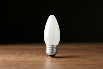 New modern lamp bulb on wooden table against black background