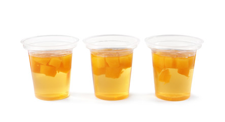 Tasty jelly desserts with slices of fruit in plastic cups on white background