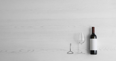 Flat lay composition with bottle of wine and elegant glass on white wooden background. Space for text
