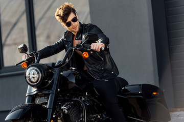 motorcyclist in leather jacket sitting on motorcycle and looking away