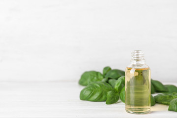 Bottle of basil essential oil on white wooden table against light background. Space for text