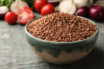 Bowl of uncooked buckwheat on wooden table, closeup