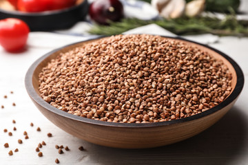 Wooden bowl of buckwheat on white table, closeup