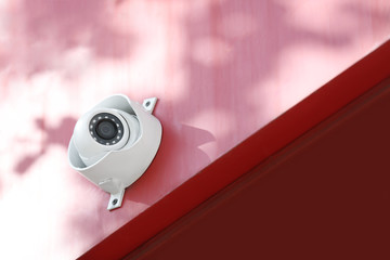 Modern CCTV security camera on red building wall outdoors. Space for text