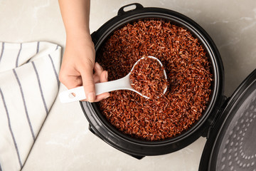 Woman taking delicious brown rice from multi cooker at table, top view