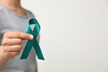 Woman holding teal awareness ribbon against light background, closeup