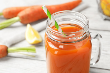 Mason jar with fresh carrot juice on white wooden table, space for text