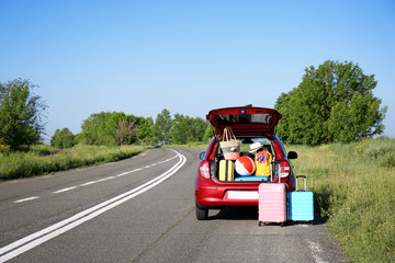Suitcases near family car with open trunk full of luggage on highway. Space for text