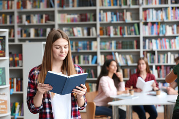 Young pretty woman reading book in library. Space for text