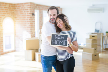 Middle age senior couple moving to a new house, smiling happy in love with apartmant holding a blackboard with new home text