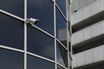 Modern building with tinted windows and CCTV camera, low angle view. Urban architecture