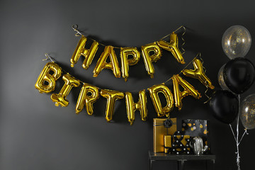 Room interior with gift boxes and phrase HAPPY BIRTHDAY made of golden balloon letters