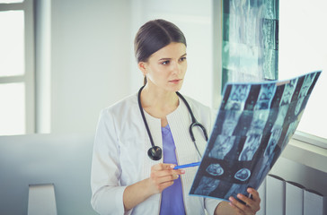Young female doctor with stethoscope pointing at X-ray at doctor's office