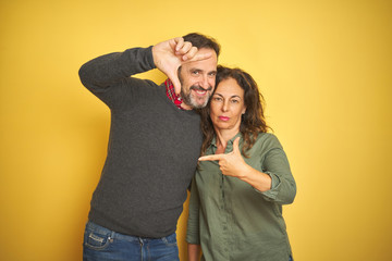 Fototapeta premium Beautiful middle age couple over isolated yellow background smiling making frame with hands and fingers with happy face. Creativity and photography concept.