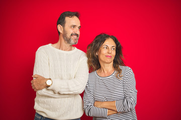 Beautiful middle age couple wearing winter sweater over isolated red background smiling looking to the side and staring away thinking.