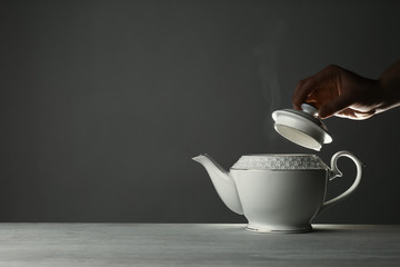 Woman removing lid from ceramic teapot at table against grey background, closeup. Space for text