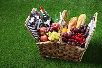 Wicker picnic basket with different products on green grass, space for text
