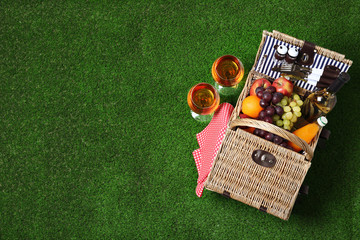 Wicker picnic basket with different products on green grass, top view. Space for text