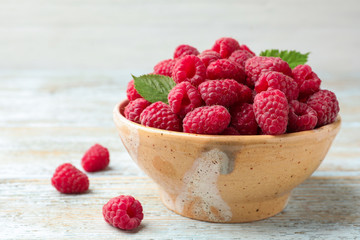 Bowl of delicious fresh ripe raspberries with leaves on wooden table, space for text