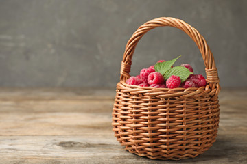Basket of delicious fresh ripe raspberries with leaves on wooden table against grey background, space for text