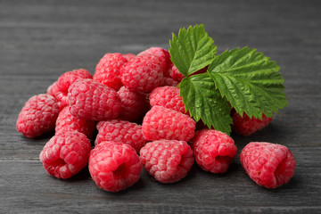 Delicious fresh ripe raspberries with leaves on dark wooden table