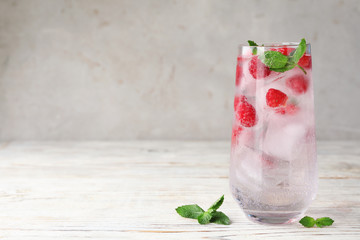 Glass of refreshing drink with raspberry and mint on light wooden table against grey background,...