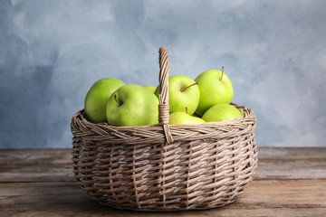 Wicker basket of fresh ripe green apples on wooden table against blue background