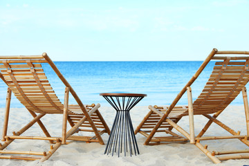 Empty wooden sunbeds and table on sandy shore. Beach accessories