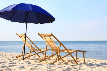Empty wooden sunbeds and umbrella on sandy shore. Beach accessories