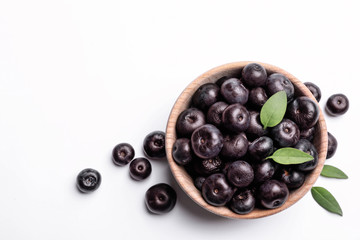 Bowl of fresh acai berries with leaves on white background, top view