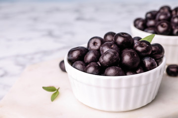 Bowl of fresh acai berries on board, closeup. Space for text