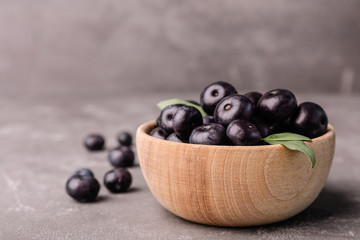 Bowl of fresh acai berries on grey stone table, closeup. Space for text