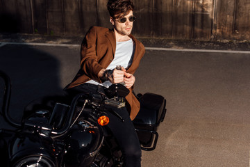 Fototapeta na wymiar handsome young man in brown jacket lying on motorcycle and holding alcohol bottle