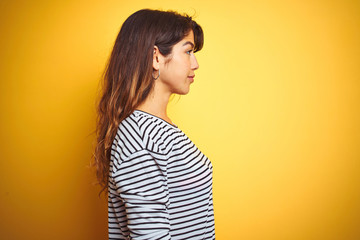 Young beautiful woman wearing stripes t-shirt standing over yelllow isolated background looking to side, relax profile pose with natural face with confident smile.