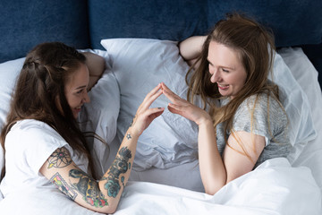two smiling lesbians touching hands and looking at each other in bed