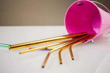 Stainless steel eco natural reusable metallic straws in a pink decorative bucket flat on a white table. Reduce plastic waste in environment, plastic free items. stop plastic pollution.