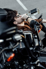selective focus of man drinking alcohol while sitting on ground and leaning on motorcycle