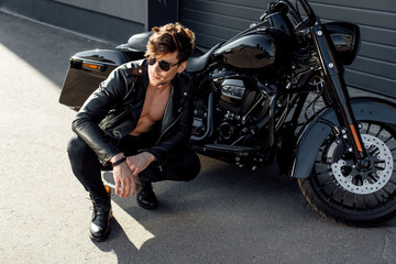 Plakat muscular young man sitting near motorcycle and looking away