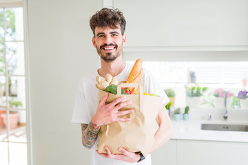 Young handsome man holding a paper bag full of fresh groceries at home