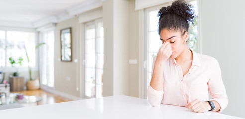 Wide angle of beautiful african american woman with afro hair tired rubbing nose and eyes feeling fatigue and headache. Stress and frustration concept.