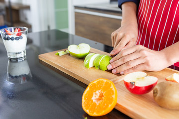 Closeup of young asian man with apron cutting red and green apple kiwi orange on wooden black table of kitchen room