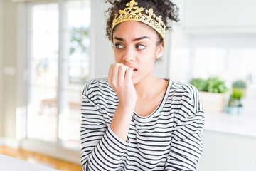 Fototapeta na wymiar Young african american girl wearing golden queen crown on head looking stressed and nervous with hands on mouth biting nails. Anxiety problem.