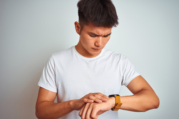 Young asian chinese man wearing t-shirt standing over isolated white background Checking the time on wrist watch, relaxed and confident