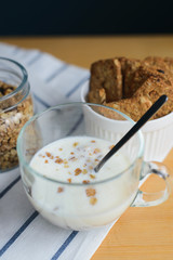 milk and cereals flakes in glass cup with granola and wholegrain cookies on striped textile napkin on wooden table, close up view from angle above of vertical still life stock photo image